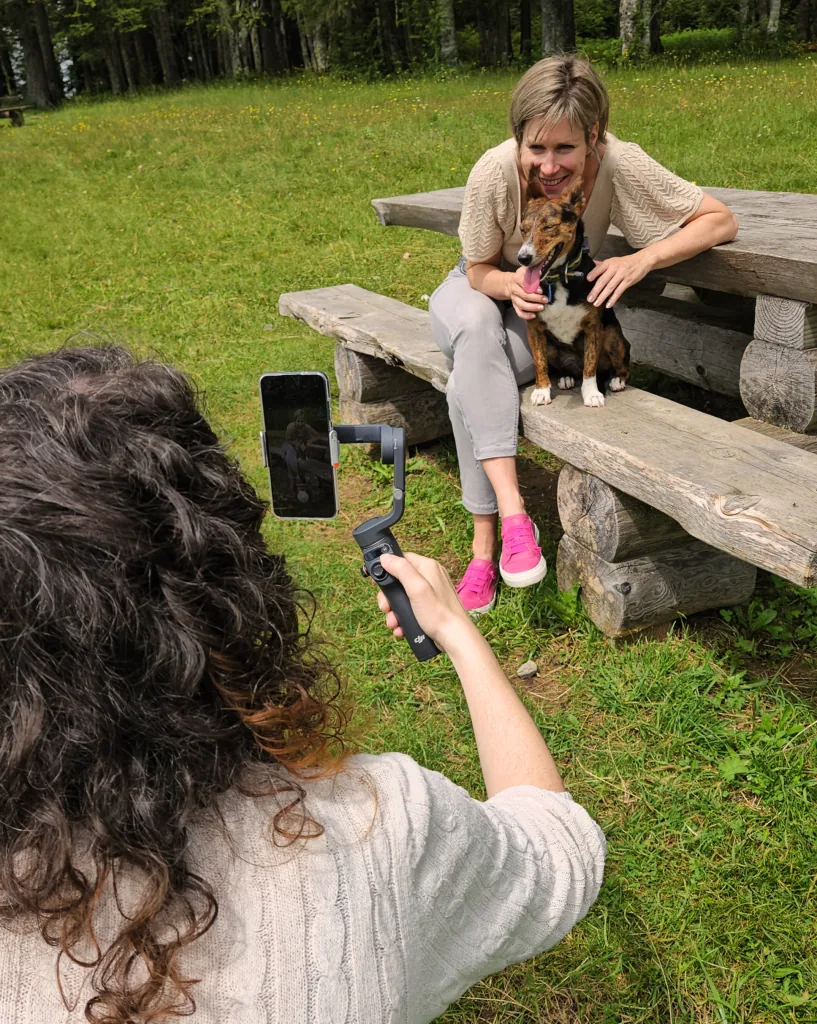 Collaboratrice d'Osmose Marketing filmant au smartphone une cliente assise sur un banc en extérieur